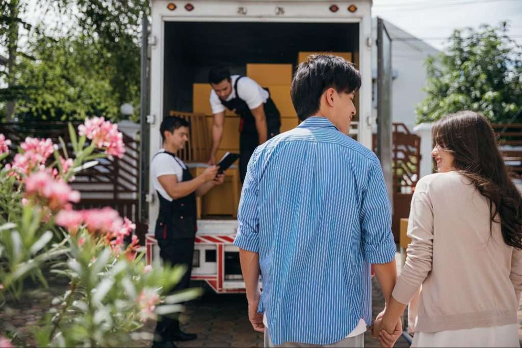 Young couple and two movers talking, smiling, and signing papers.